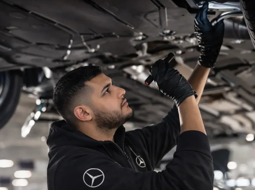 Mecânico especialista com uniforme Mercedes-Benz inspecionando suspensão e parte inferior de veículo Mercedes elevado na rampa com lanterna na oficina Premium Car em Porto Alegre