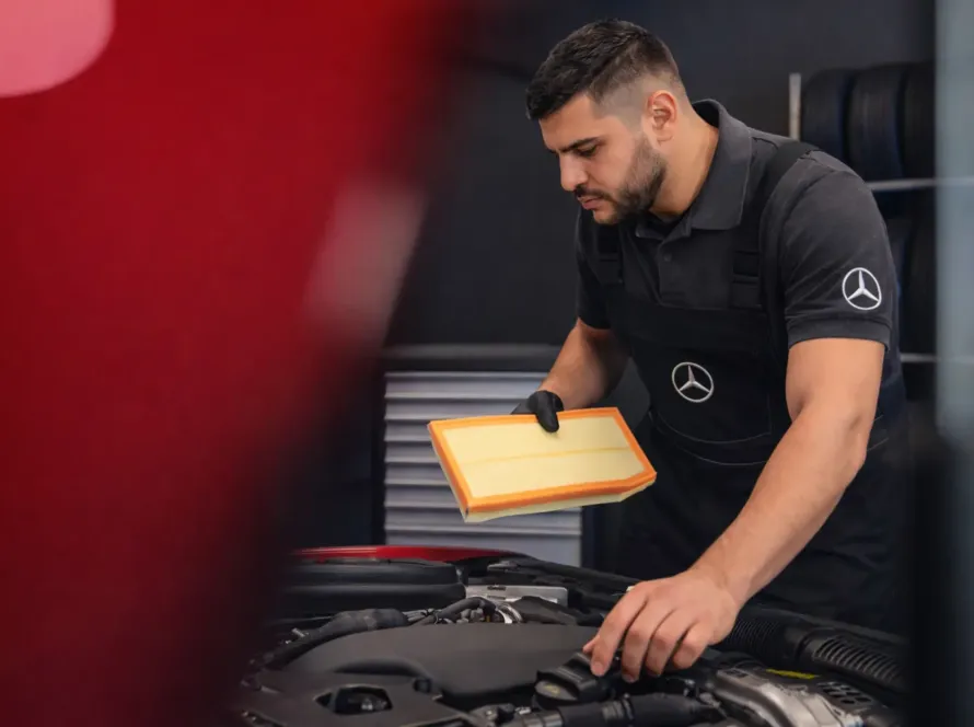 Mecânico especialista com uniforme Mercedes-Benz trocando filtro de ar no motor de Mercedes vermelho com capô aberto na oficina Premium Car em Porto Alegre