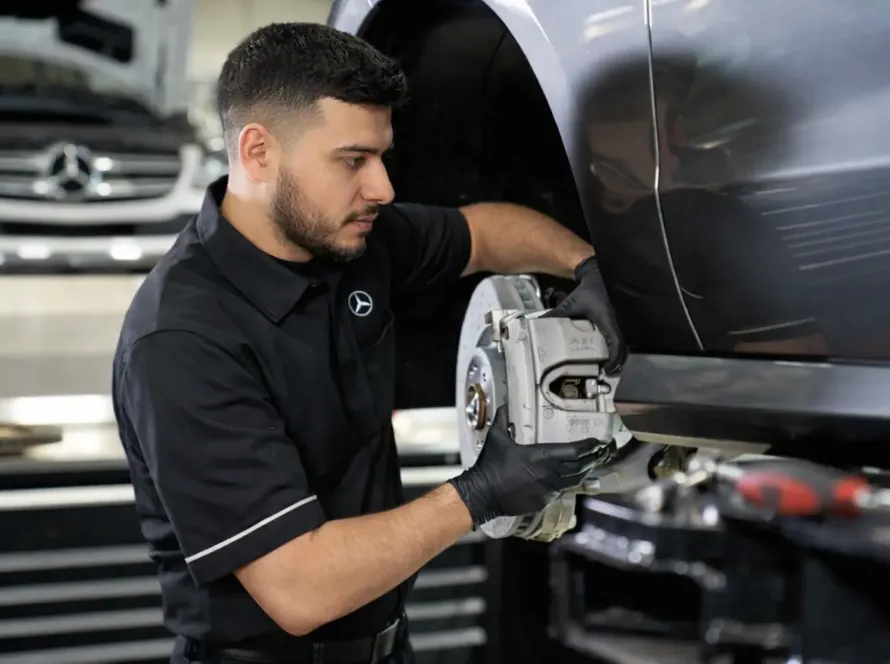 Mecânico especialista com uniforme Mercedes-Benz realizando troca de freio em veículo Mercedes cinza elevado na oficina Premium Car em Porto Alegre