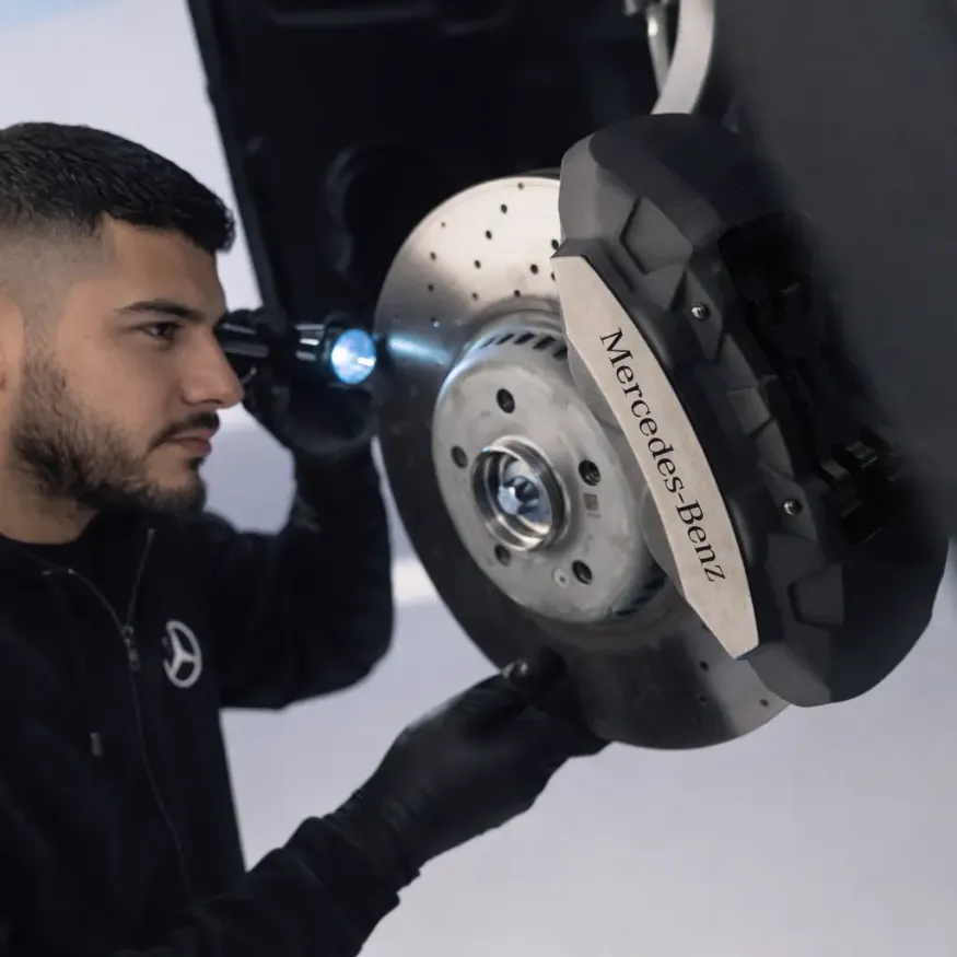 Mecânico especialista com uniforme Mercedes-Benz inspecionando suspensão e parte inferior de veículo Mercedes elevado na rampa com lanterna na oficina Premium Car em Porto Alegre